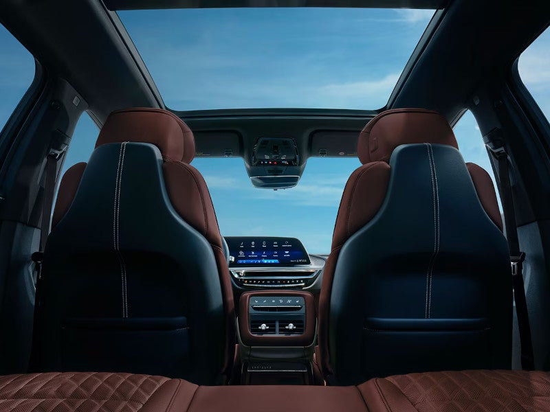 Interior view from the rear seat of a Cadillac Lyriq showing brown leather seats, a panoramic roof, and a curved display.