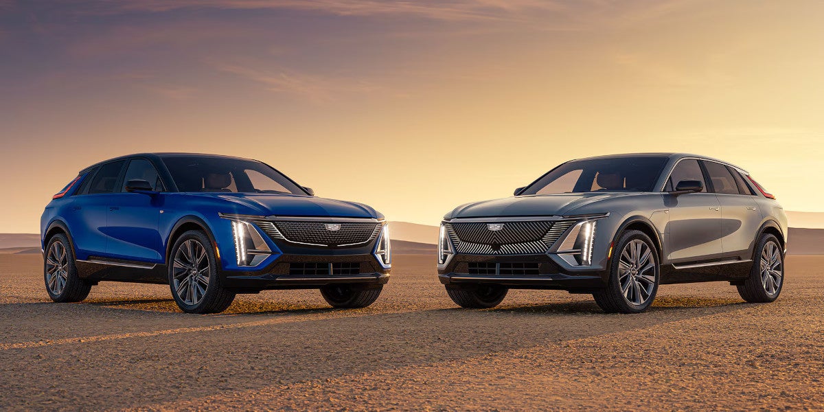 Blue and silver Cadillac Lyriq electric SUVs parked facing each other in the desert at sunset.